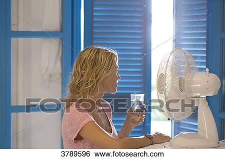 Young woman in profile in front a fan with a glass of water. View Large Photo Image Stock Photograph - Young woman in profile in front a fan with a glass of water.. Fotosearch