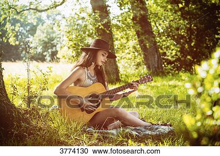 Young woman sitting in the grass plays guitar View Large Photo Image Stock Image - Young woman sitting in the grass plays guitar. Fotosearch