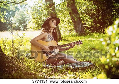 Young woman sitting in the grass plays guitar View Large Photo Image Stock Image - Young woman sitting in the grass plays guitar. Fotosearch
