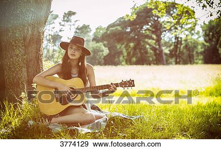 Young woman sitting in the grass plays guitar View Large Photo Image Stock Photo - Young woman sitting in the grass plays guitar. Fotosearch