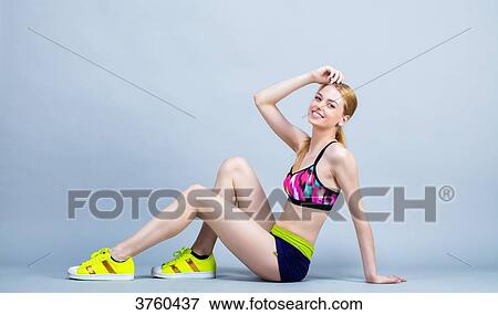 Stock Photo - Young woman sitting, smiling, dressed in fitness, looking at the camera. Fotosearch
