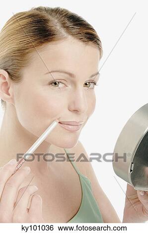 Young Woman face making-up her mouth with a pen, little mirror in her hand, close-up (studio) View Large Photo Image Stock Photograph - Young Woman face making-up her mouth with a pen, little mirror in her hand, close-up (studio). Fotosearch