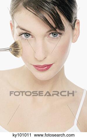 Stock Image - Young Woman face making-up with a brush, close-up (studio). Fotosearch