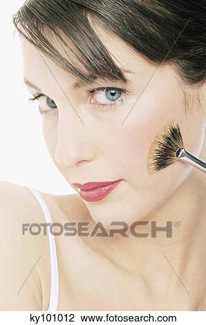 Stock Image - Young Woman face making-up with a brush, close-up (studio). Fotosearch