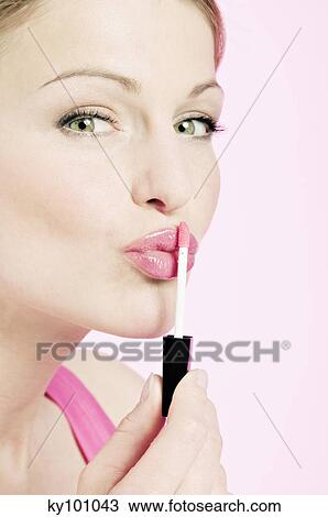 Stock Image - Young Woman face making-up with a lipstick, close-up (studio). Fotosearch
