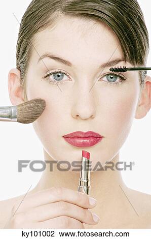 Stock Image - Young Woman face with Make-Up, a pencil, lipstick and a brush in front of her, close-up (studio). Fotosearch
