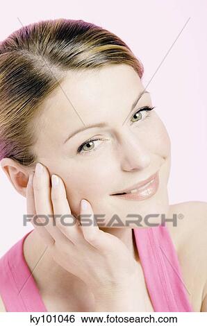 Young Woman face with make up, looking at the camera, smiling, hand on her cheek, close-up (studio) View Large Photo Image Stock Photograph - Young Woman face with make up, looking at the camera, smiling, hand on her cheek, close-up (studio). Fotosearch