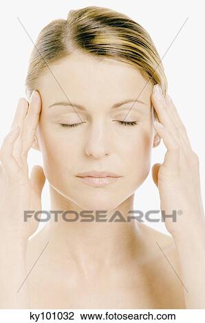 Stock Image - Young Woman face with make up, shut eyes, putting her hands on her temples (studio). Fotosearch