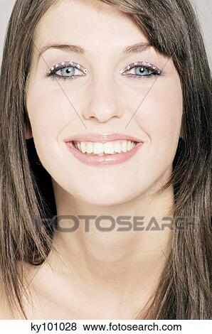 Stock Photo - Young Woman face with make up, smiling, looking at he camera, close-up (studio). Fotosearch
