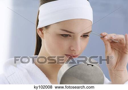 Woman plucking her eyebrow, holding a little mirror (studio) View Large Photo Image Stock Photo - Woman plucking her eyebrow, holding a little mirror (studio). Fotosearch