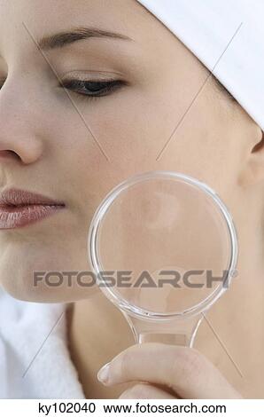 Stock Image - Woman with a magnifying glass, close up (studio). Fotosearch