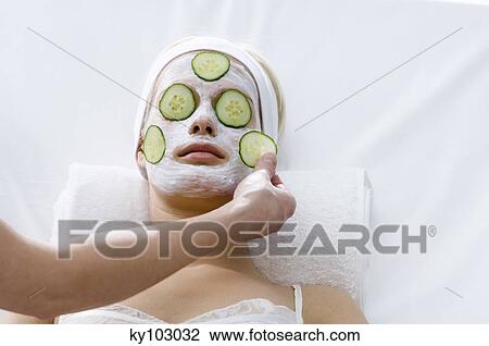 Stock Image - Portrait of a young woman with beauty mask on her face and slices cucumber on her eyes. Fotosearch
