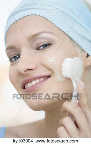 Young Woman face looking at the camera, cleaning her cheeks with a brush, close-up (studio) View Large Photo Image Picture - Young Woman face looking at the camera, cleaning her cheeks with a brush, close-up (studio). Fotosearch