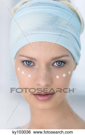 Stock Photograph - Young Woman face looking at the camera, drops of cream under her eyes, close-up (studio). Fotosearch