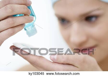 Stock Photography - Young Woman face pouring on lotion in her hand, close-up (studio). Fotosearch