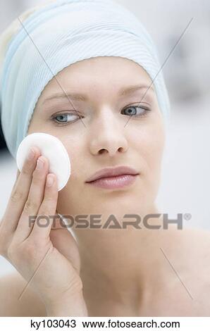 Stock Image - Young Woman face using a cleansing cotton on her cheek, close-up (studio). Fotosearch