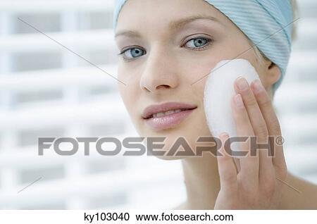 Stock Image - Young Woman face with make up, holding a bath sponge on her cheek (studio). Fotosearch