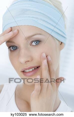 Stock Photography - Young Woman face with make up, looking at the camera, figers on her face, close-up (studio). Fotosearch