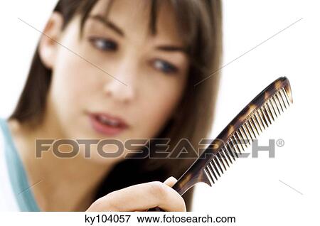Stock Photo - Portrait of a young woman combing her hair, close up (studio). Fotosearch