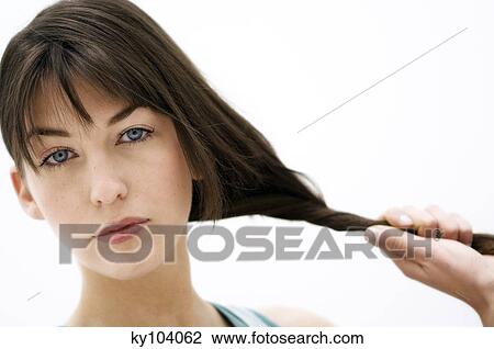 Stock Image - Portrait of a young woman holding her hair, (studio). Fotosearch