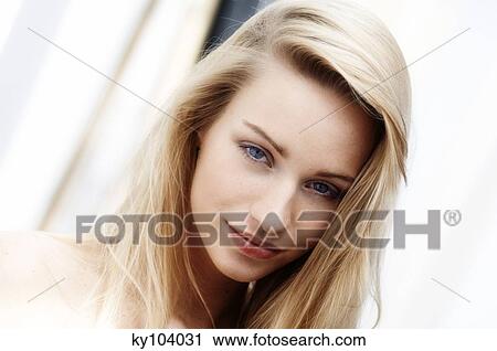 Stock Image - Portrait of a young woman looking at the camera, blond hair, close up (studio). Fotosearch