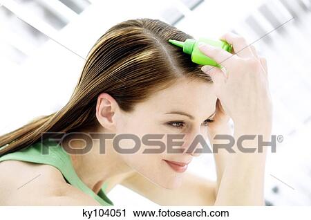 Stock Image - Portrait of a young woman pouring on hair lotion on her head. Fotosearch