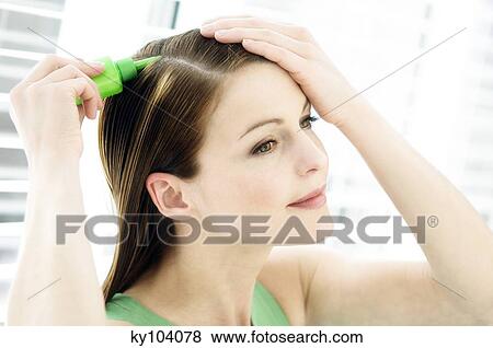Stock Photo - Portrait of a young woman pouring on hair lotion on her head. Fotosearch