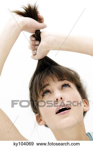 Stock Photo - Portrait of a young woman pulling her hair, close up (studio). Fotosearch