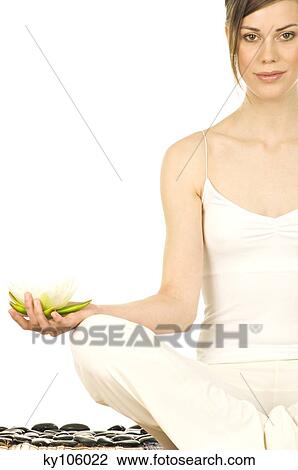 Stock Image - Young woman sitting in profile, yoga attitude, water lily in her hand. Fotosearch
