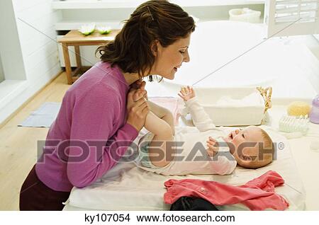 Picture - Mother dressing her baby. Fotosearch