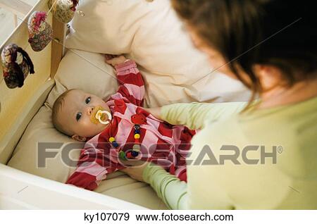 Stock Photo - Mother putting her baby in bed, comforter. Fotosearch