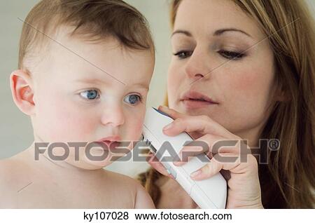 Stock Photo - Mother taking her baby's temperature with an ear-thermometer. Fotosearch