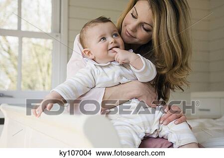 Woman and baby smiling, sitting on th bed View Large Photo Image Picture - Woman and baby smiling, sitting on th bed. Fotosearch