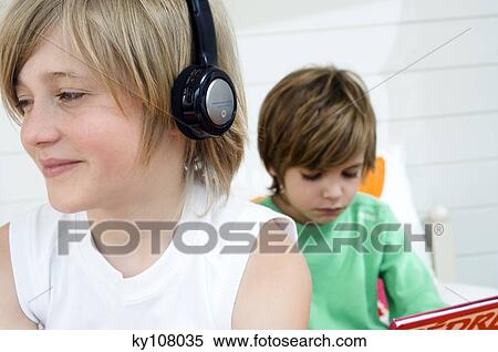 2 boys at home, one wearing headphones, the other reading in background View Large Photo Image Stock Photography - 2 boys at home, one wearing headphones, the other reading in background. Fotosearch