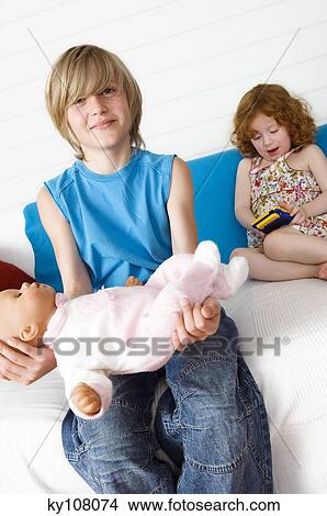 2 children at home, boy holding doll, girl playing video game View Large Photo Image Picture - 2 children at home, boy holding doll, girl playing video game. Fotosearch