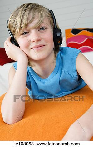 Boy lying on a bed, wearing headphones View Large Photo Image Stock Image - Boy lying on a bed, wearing headphones. Fotosearch