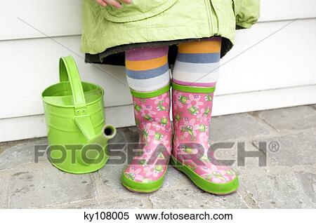 Stock Photography - Little girl in boots, close-up, green watering can. Fotosearch