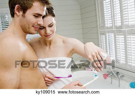 Stock Photography - Couple in a bathroom squeezing toothpaste onto toothbrushes. Fotosearch
