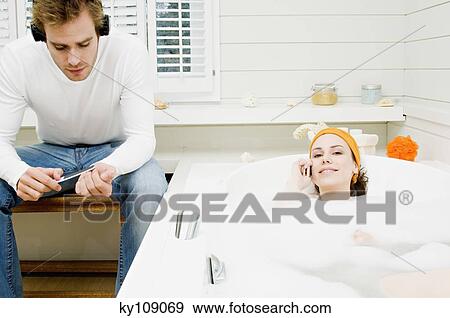Couple in bathroom, woman phoning in bath, man with headphones filing his nails View Large Photo Image Stock Photo - Couple in bathroom, woman phoning in bath, man with headphones filing his nails. Fotosearch
