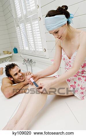 Stock Image - Man having a bath and woman in nightgown filing her nails. Fotosearch