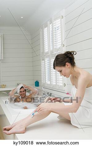 Man having a bath and woman wrapped in a towel shaving her legs View Large Photo Image Stock Photo - Man having a bath and woman wrapped in a towel shaving her legs. Fotosearch