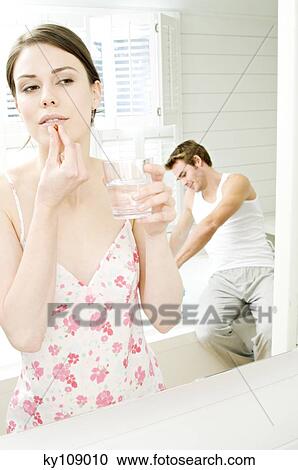 Woman in nightgown swallowing pill in front of bathroom mirror, man sitting on tub edge in background View Large Photo Image Stock Image - Woman in nightgown swallowing pill in front of bathroom mirror, man sitting on tub edge in background. Fotosearch