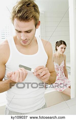 Young man filing his nails in front of bathroom mirror, woman sitting on tub edge in background View Large Photo Image Stock Photo - Young man filing his nails in front of bathroom mirror, woman sitting on tub edge in background. Fotosearch