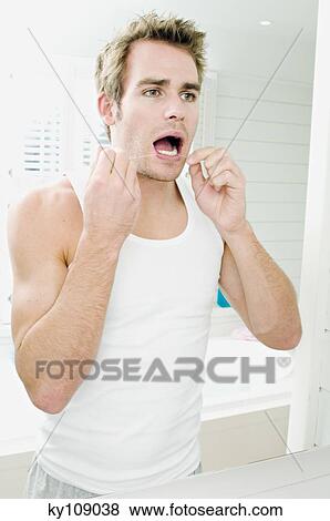 Young man flossing teeth in front of bathroom mirror View Large Photo Image Stock Photo - Young man flossing teeth in front of bathroom mirror. Fotosearch