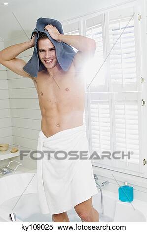 Young man wrapped in a towel, standing in bath towelling hair, smiling for the camera View Large Photo Image Stock Photography - Young man wrapped in a towel, standing in bath towelling hair, smiling for the camera. Fotosearch