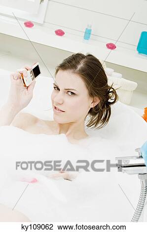Young woman having a bath, holding mobile phone View Large Photo Image Stock Image - Young woman having a bath, holding mobile phone. Fotosearch