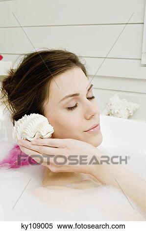 Young woman in bath, holding a shell to her ear View Large Photo Image Stock Photography - Young woman in bath, holding a shell to her ear. Fotosearch