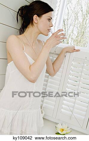 Young woman in white robe drinking glass of water, looking through window View Large Photo Image Stock Image - Young woman in white robe drinking glass of water, looking through window. Fotosearch