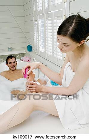 Stock Photo - Young woman wrapped in a towel, giving pedicure to man in bath. Fotosearch