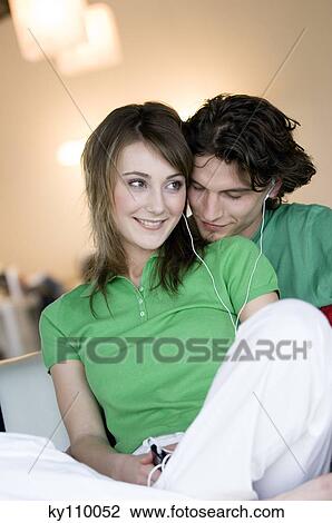 Stock Image - Couple embracing, wearing earphones. Fotosearch